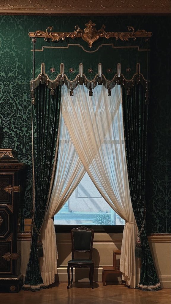 Victorian-style room with intricate green wallpaper and classic furniture, featuring elaborate curtains.