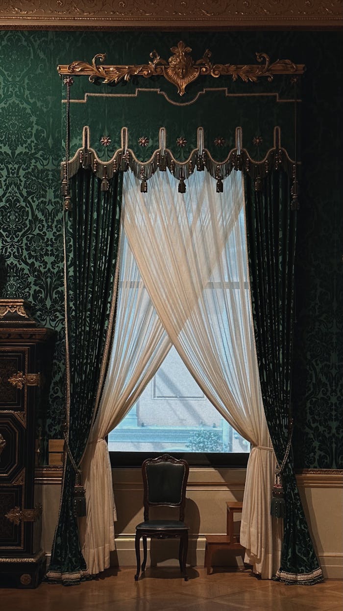 Victorian-style room with intricate green wallpaper and classic furniture, featuring elaborate curtains.